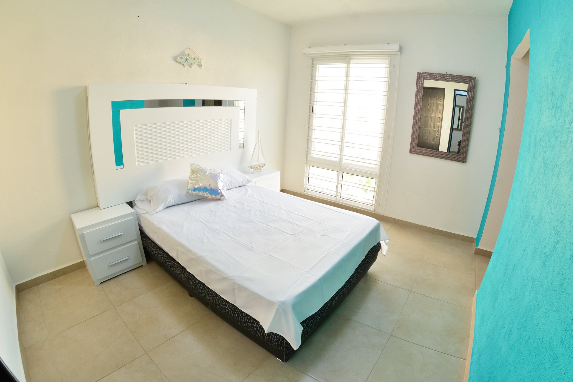 Minimalist bedroom with white bed, turquoise accents, white nightstand, and matching headboard in bright, modern space