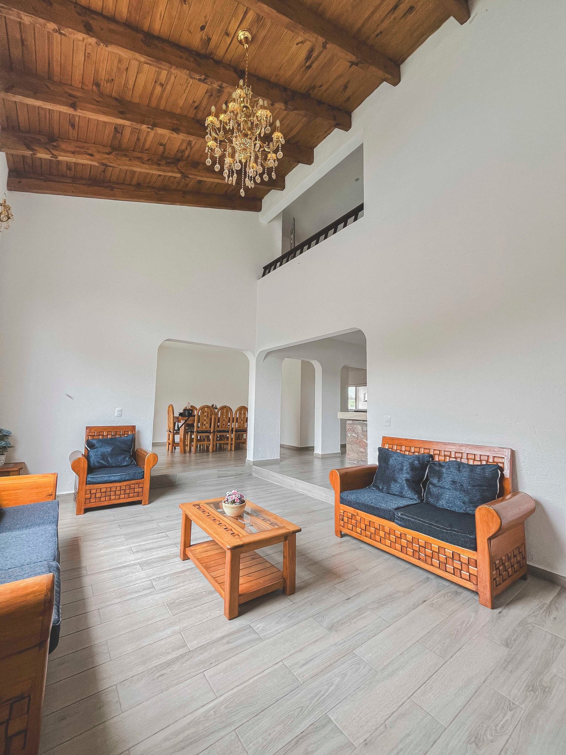Spacious living room with wooden beamed ceiling, orange and blue upholstered furniture, wooden coffee table, and crystal chandelier.
