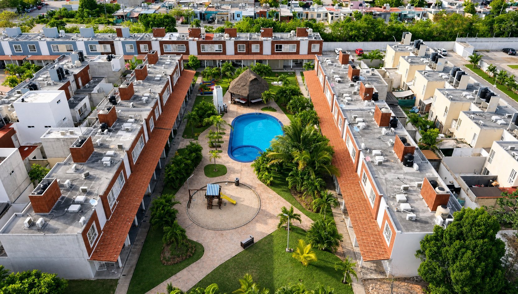Aerial view of residential complex with modern brick buildings surrounding a central courtyard featuring a blue swimming pool and landscaped gardens