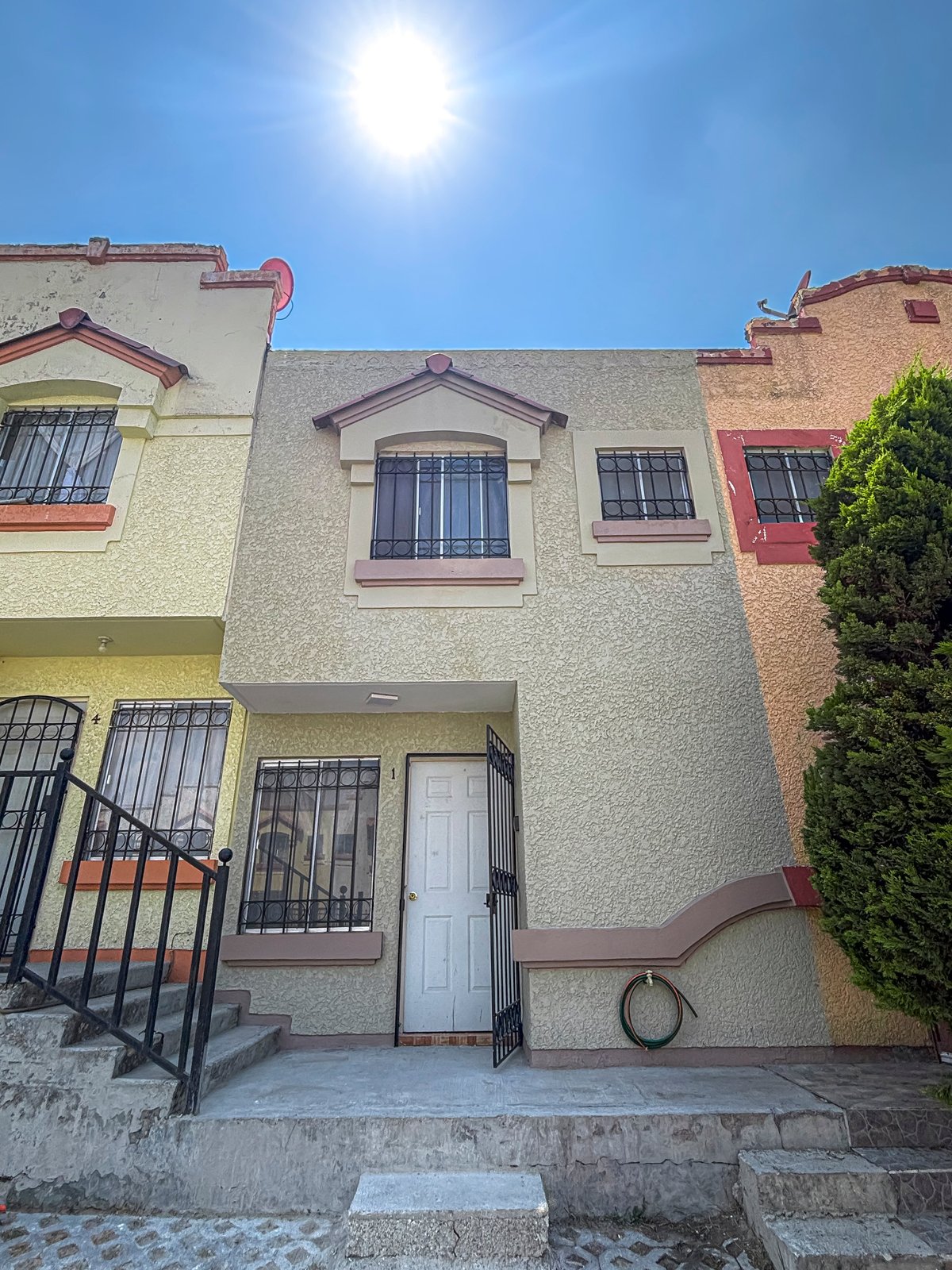 Two-story townhouse with cream and terra cotta colored facade, black-barred windows, and front entrance under bright blue sky