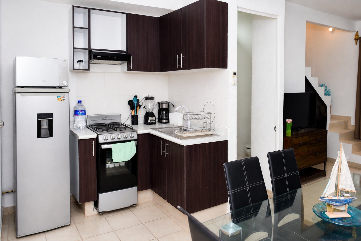 Modern kitchen with dark wood cabinets, white appliances, stovetop, and black checkered dining chairs.