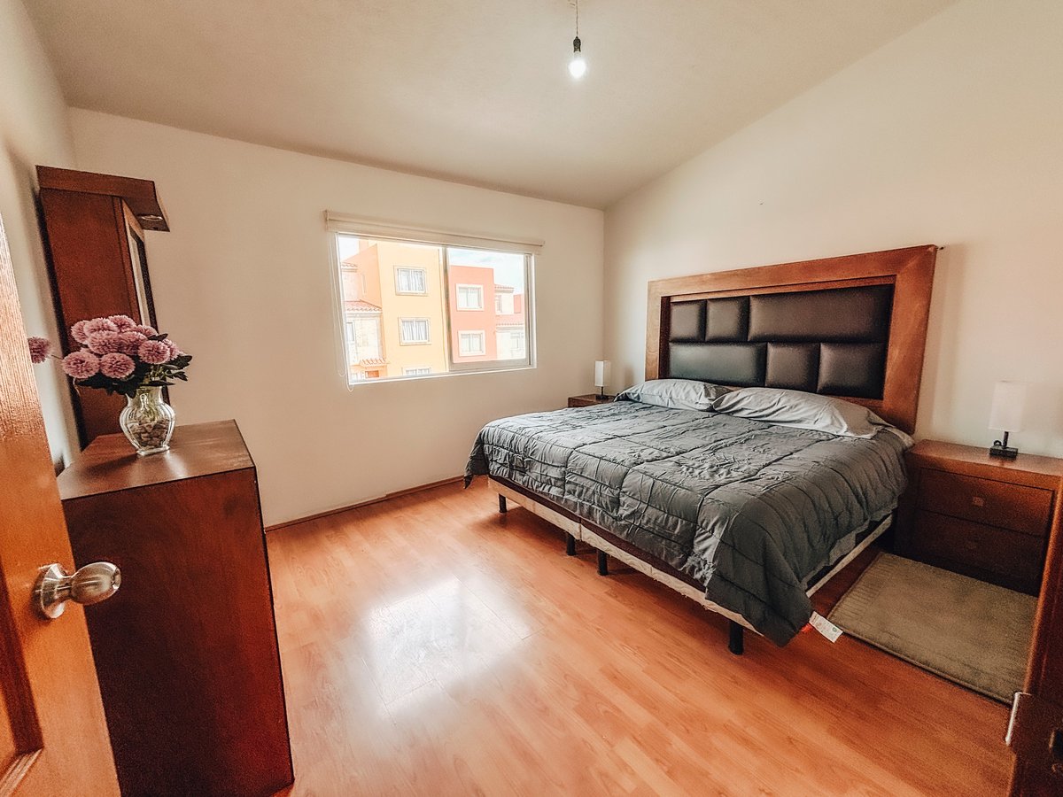 Spacious bedroom with wooden furniture, a bed with gray bedding, hardwood flooring, and a window overlooking apartment buildings