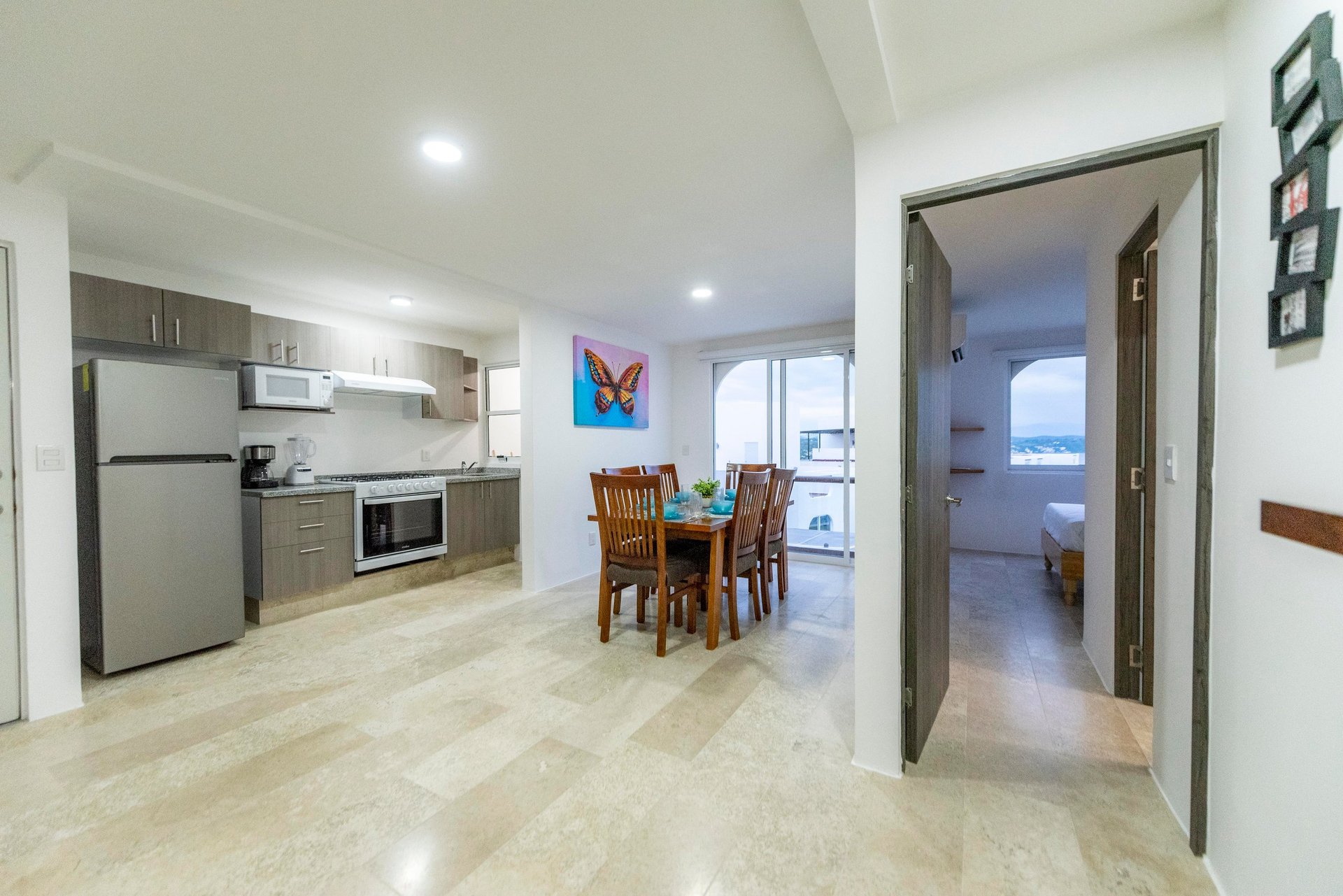 Modern open-plan apartment interior with kitchen, dining area, and hallway leading to other rooms, featuring light wood flooring and contemporary furnishings.