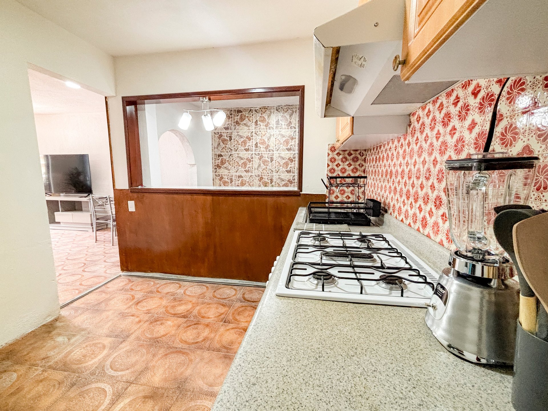 Vintage kitchen with gas stove, patterned wallpaper, and retro flooring, featuring wood cabinetry and period furnishings