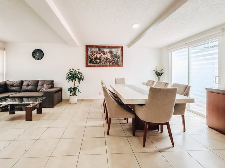 Modern open-plan living and dining room with cream tile flooring, gray sectional sofa, white dining table, beige chairs, and bright windows