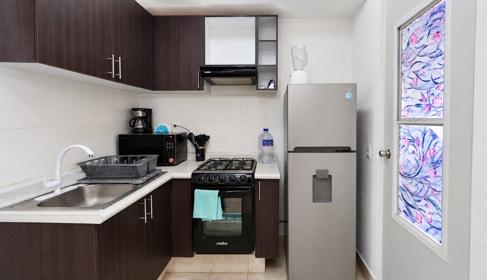 Modern compact kitchen with dark wood cabinets, stainless steel refrigerator, gas stove, and decorative purple wall art.