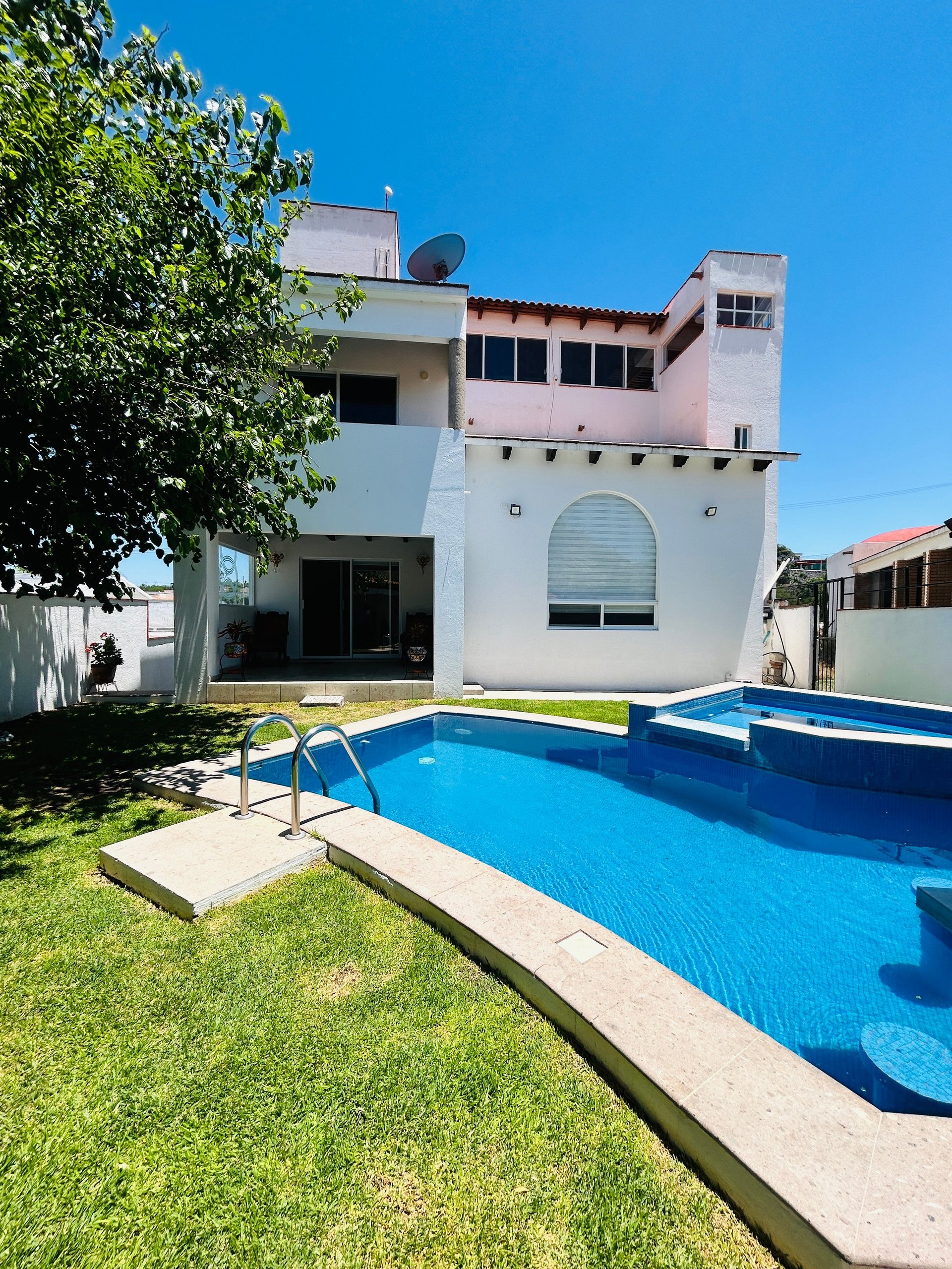Modern white residential house with blue swimming pool, green lawn, and metal ladder on a clear sunny day