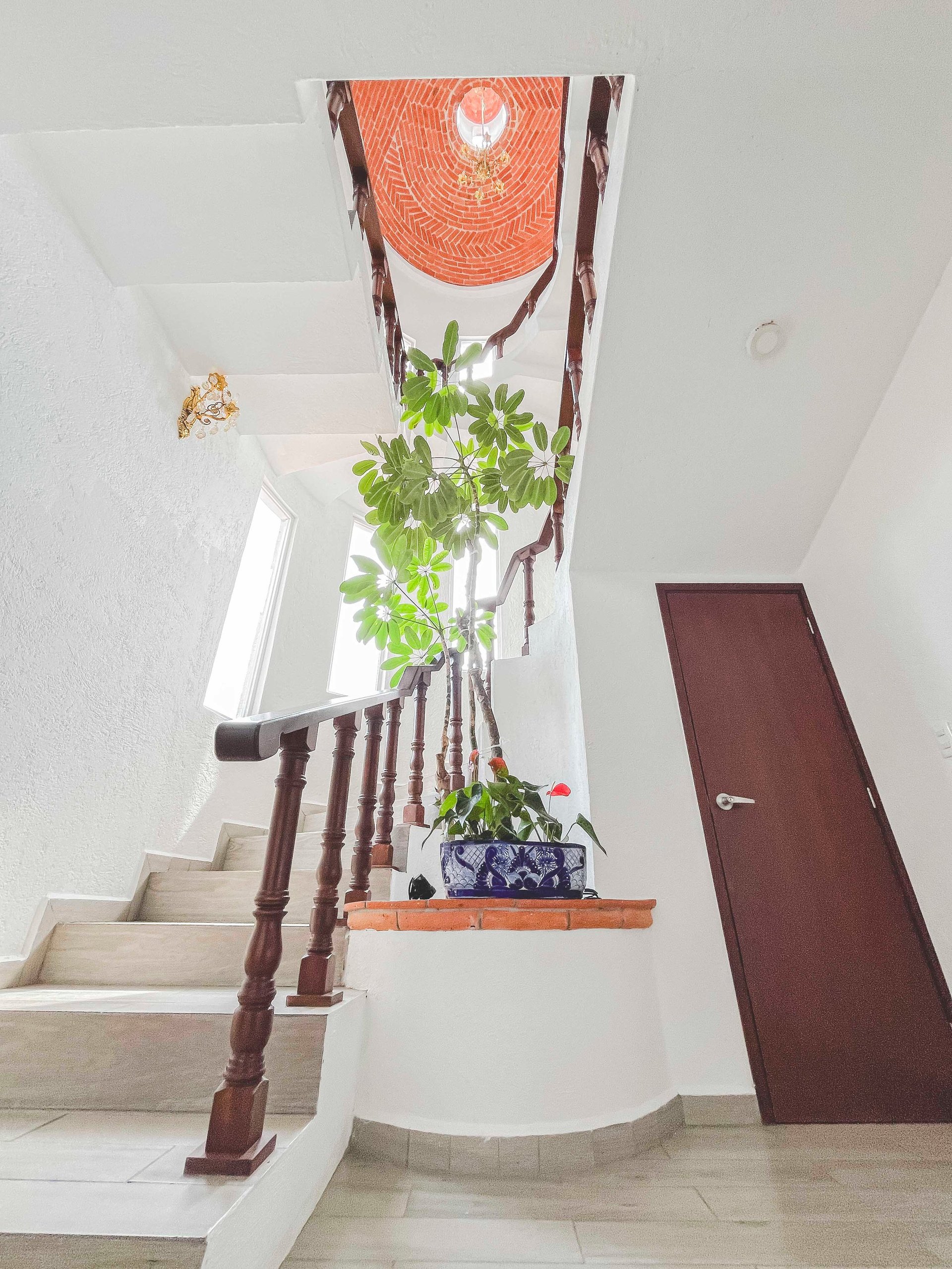 Staircase landing with hanging potted plant, decorative orange macramé wall hanging, and wooden railings