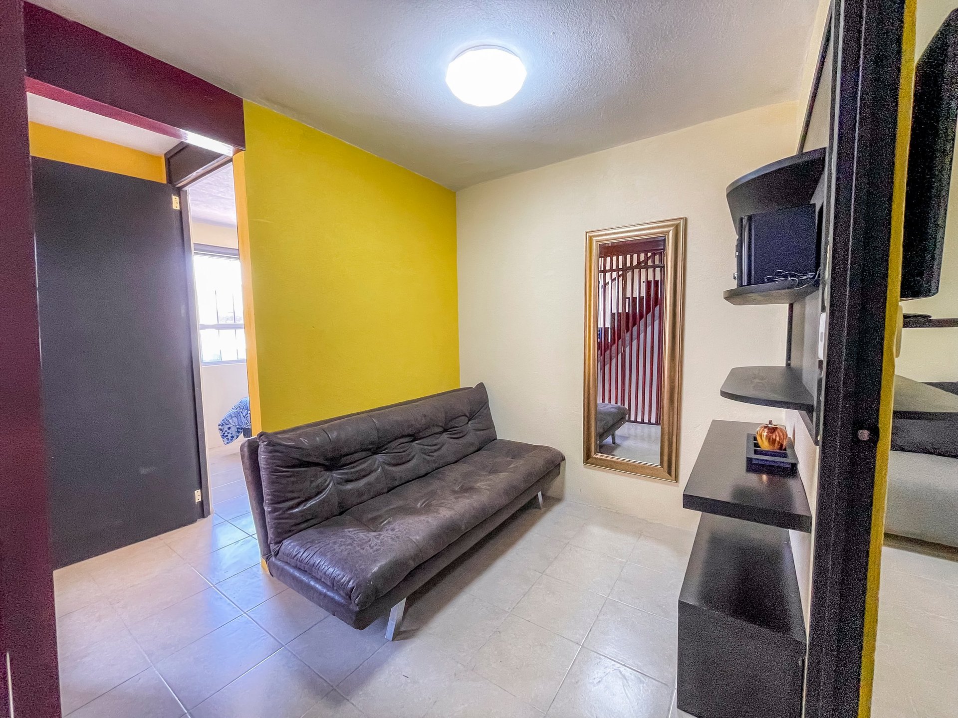 Modern room with bright yellow wall, black futon sofa, and burgundy door frame with ceiling light
