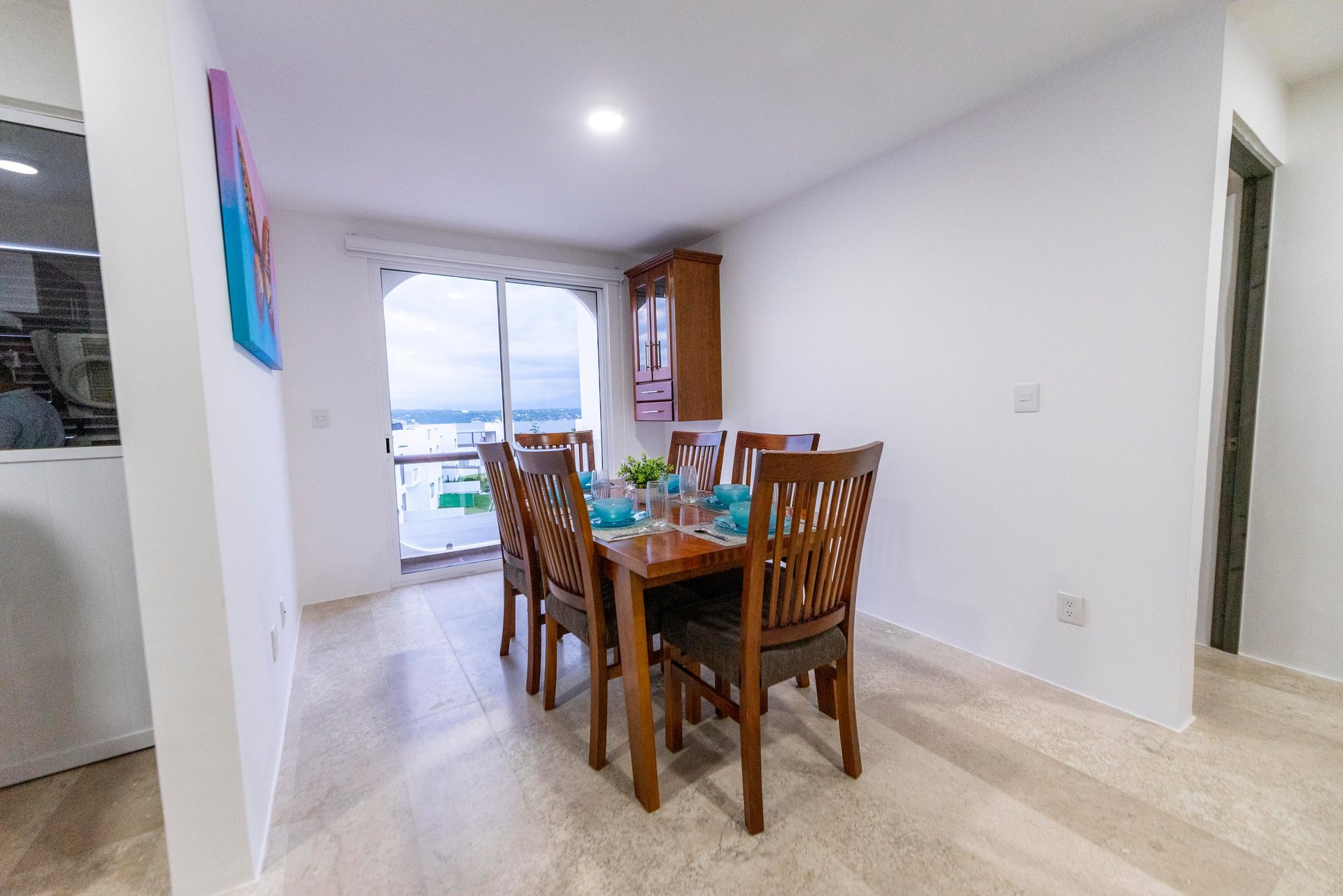 Modern dining room with wooden table and chairs, overlooking a balcony with ocean view, minimalist decor
