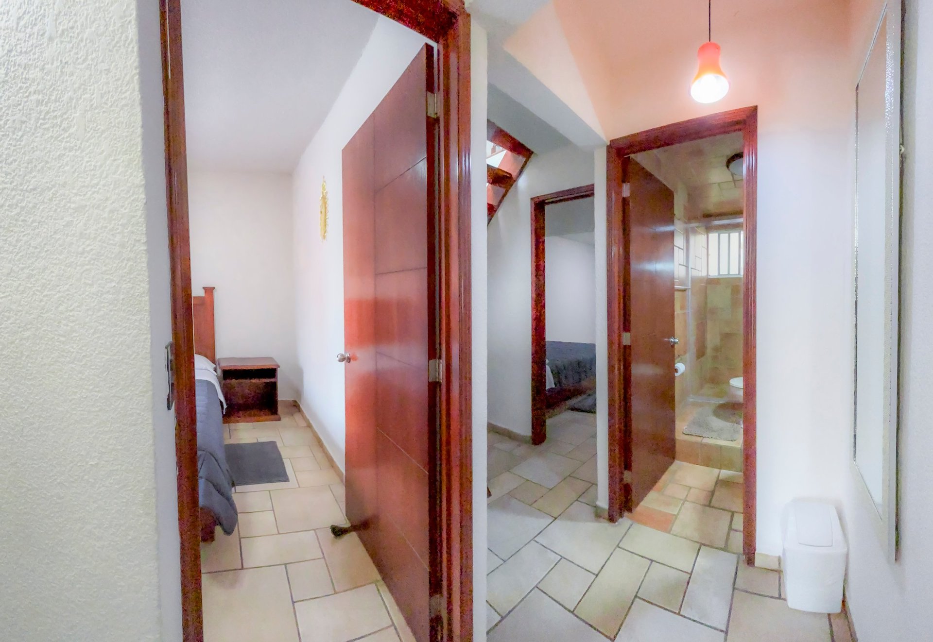 Narrow hallway with red wooden doors leading to different rooms, white walls, and tile flooring.