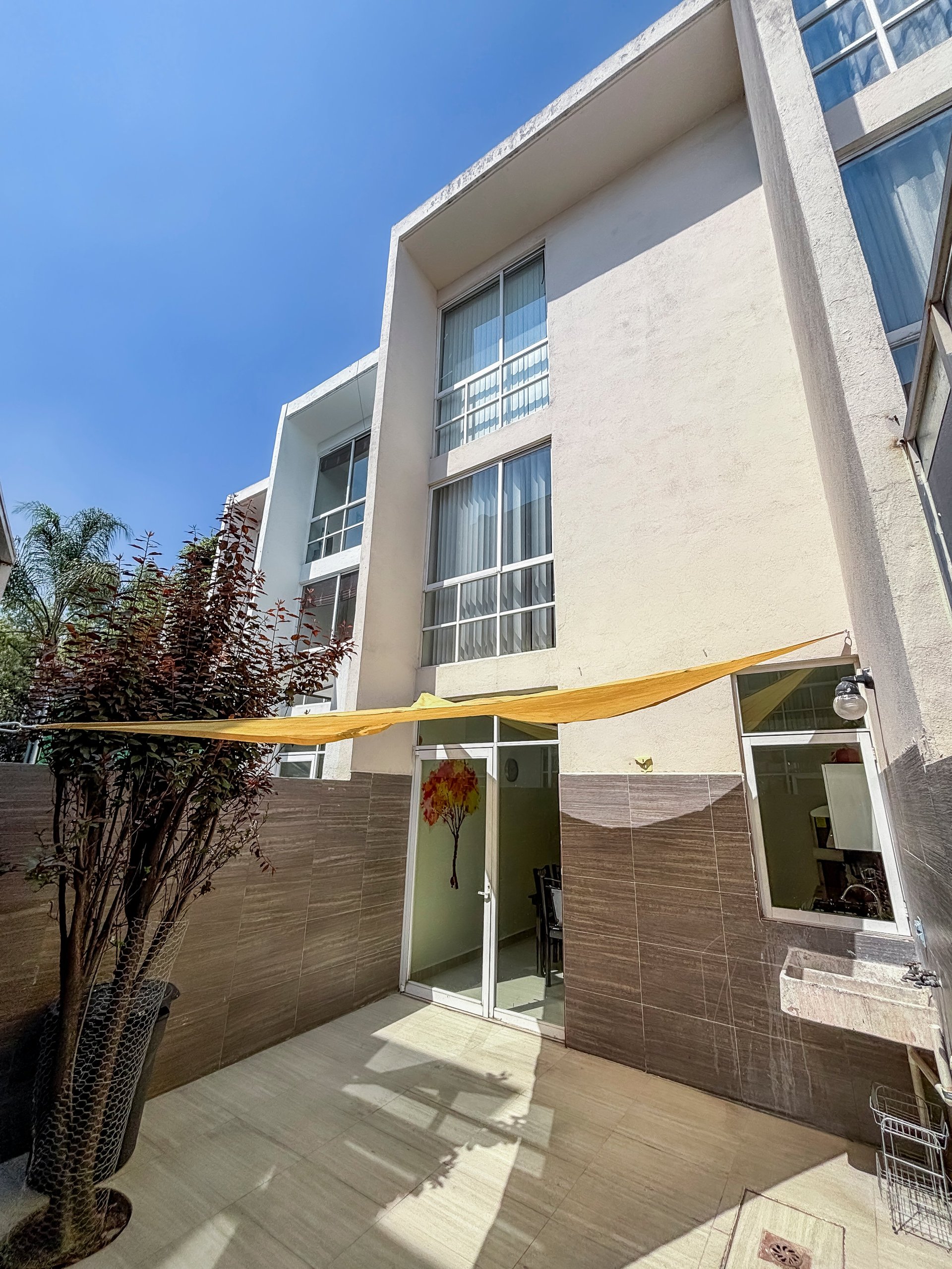 Modern white residential building with yellow shade sail over patio entrance on sunny day