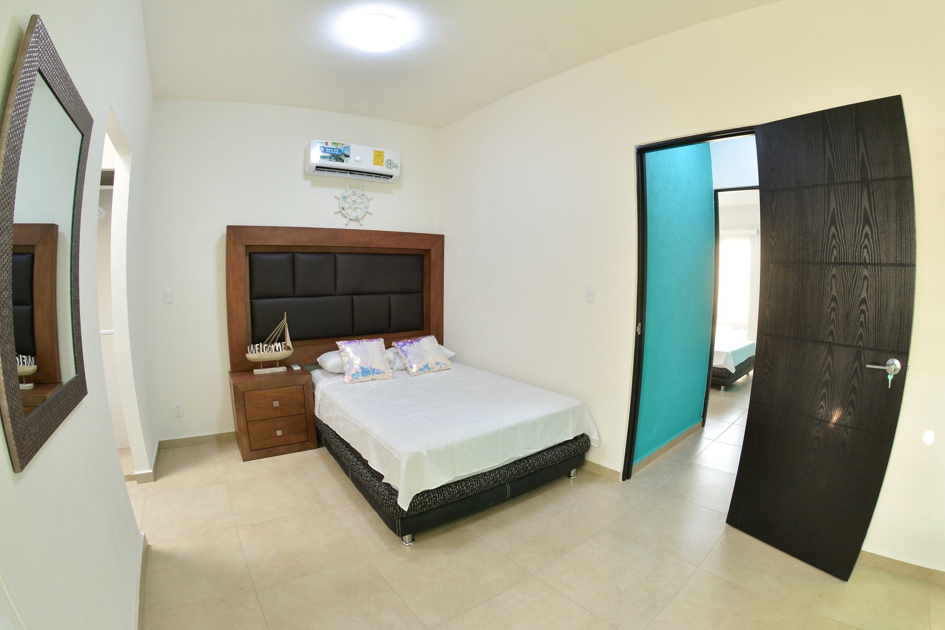 Modern hotel bedroom with wooden bed frame, white bedding, wooden nightstand, and black door with turquoise trim