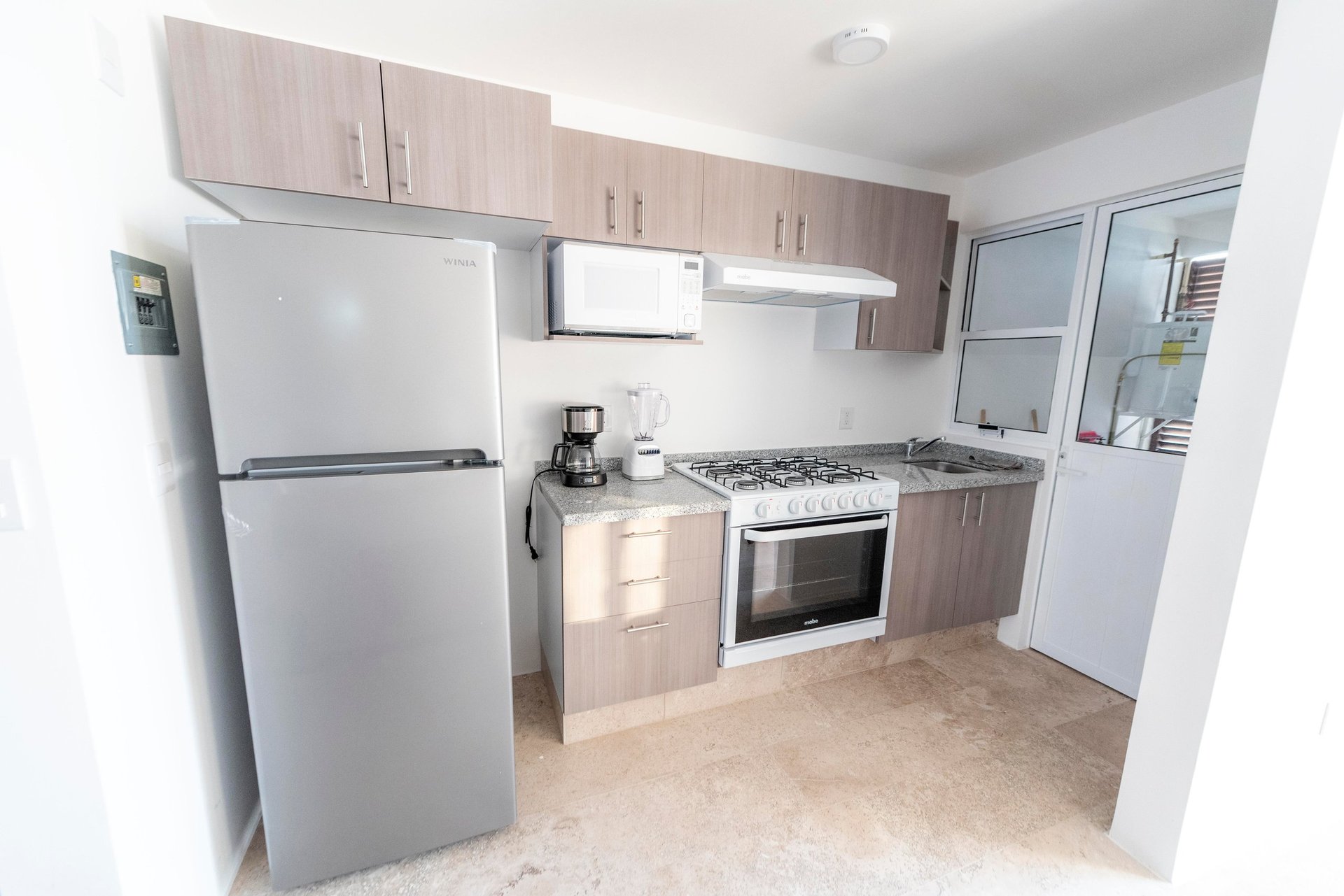 Modern kitchen with white appliances, light wood cabinetry, gas range, and tile flooring