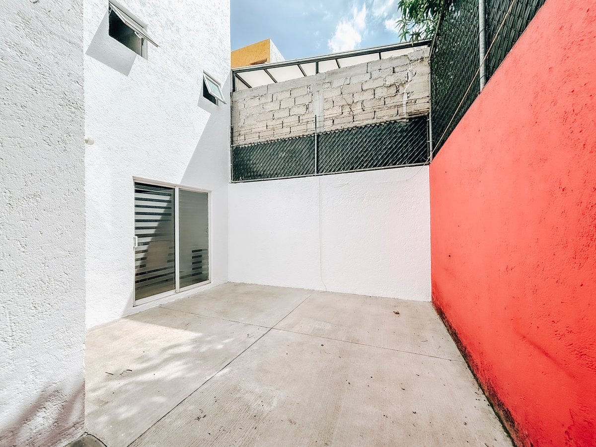 Empty concrete courtyard with white and coral red walls, green metal railing above, and blue sky visible overhead