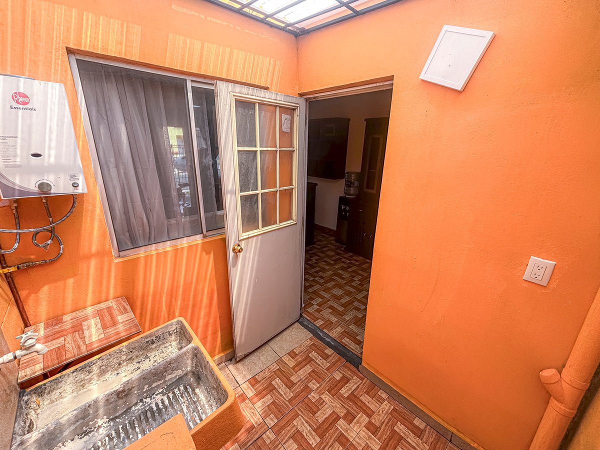 Interior of a small orange room with corrugated metal walls, a water heater on the left, open doorway, and herringbone tile flooring
