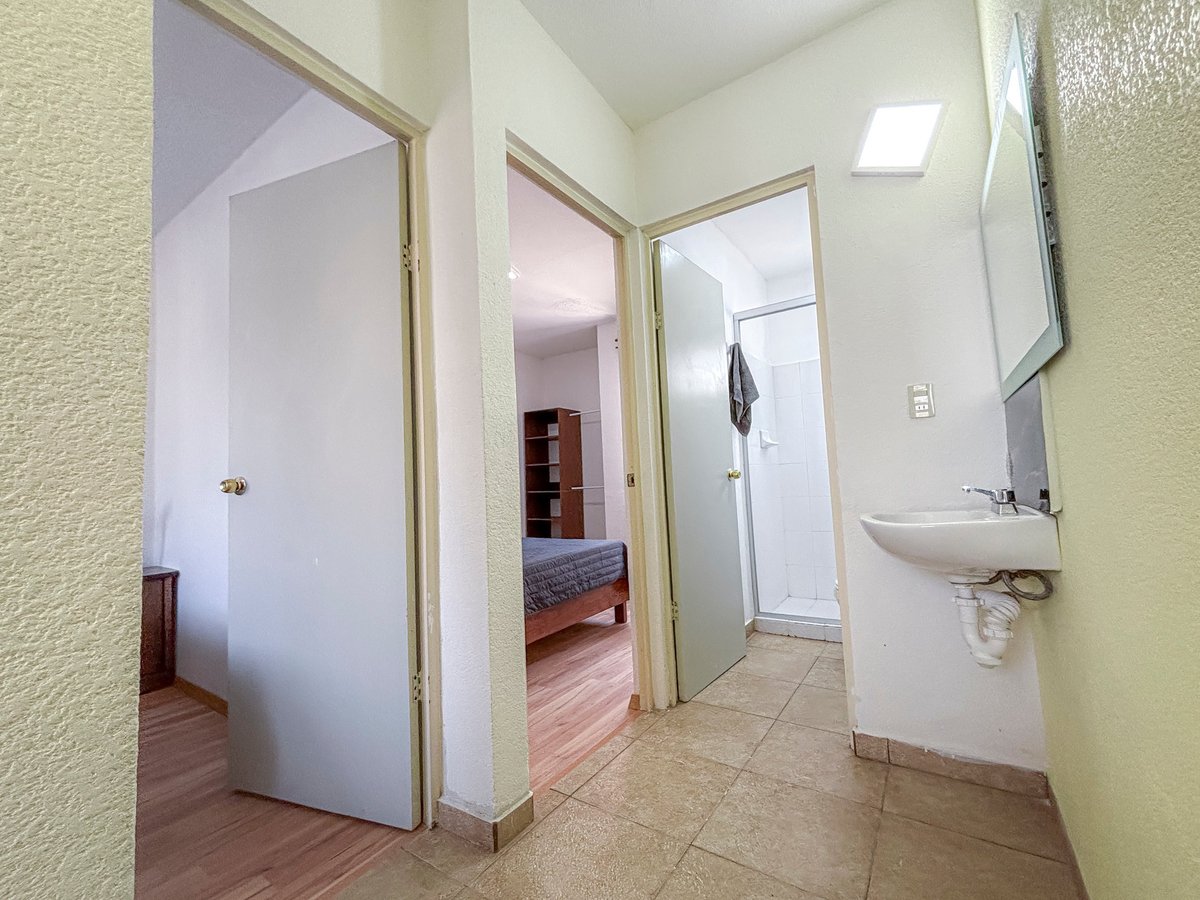 Hallway with white doors opening to bedroom and bathroom, beige walls, tiled flooring, and white sink on right wall
