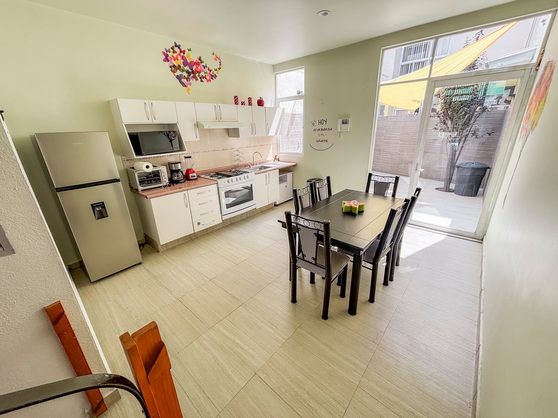 Bright modern kitchen with white cabinets, stainless appliances, and a dining table with black chairs overlooking a patio