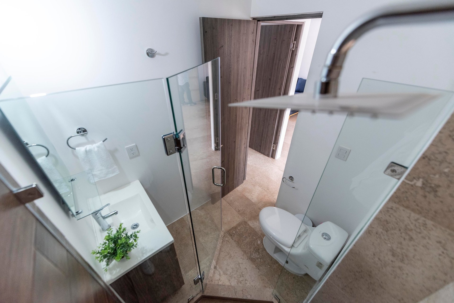 Overhead view of a modern bathroom with glass shower enclosure, white sink vanity, and toilet, with wooden curtains visible through doorway.