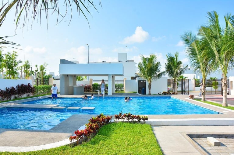Modern white pool house with large blue swimming pool, palm trees, and people swimming on a sunny day