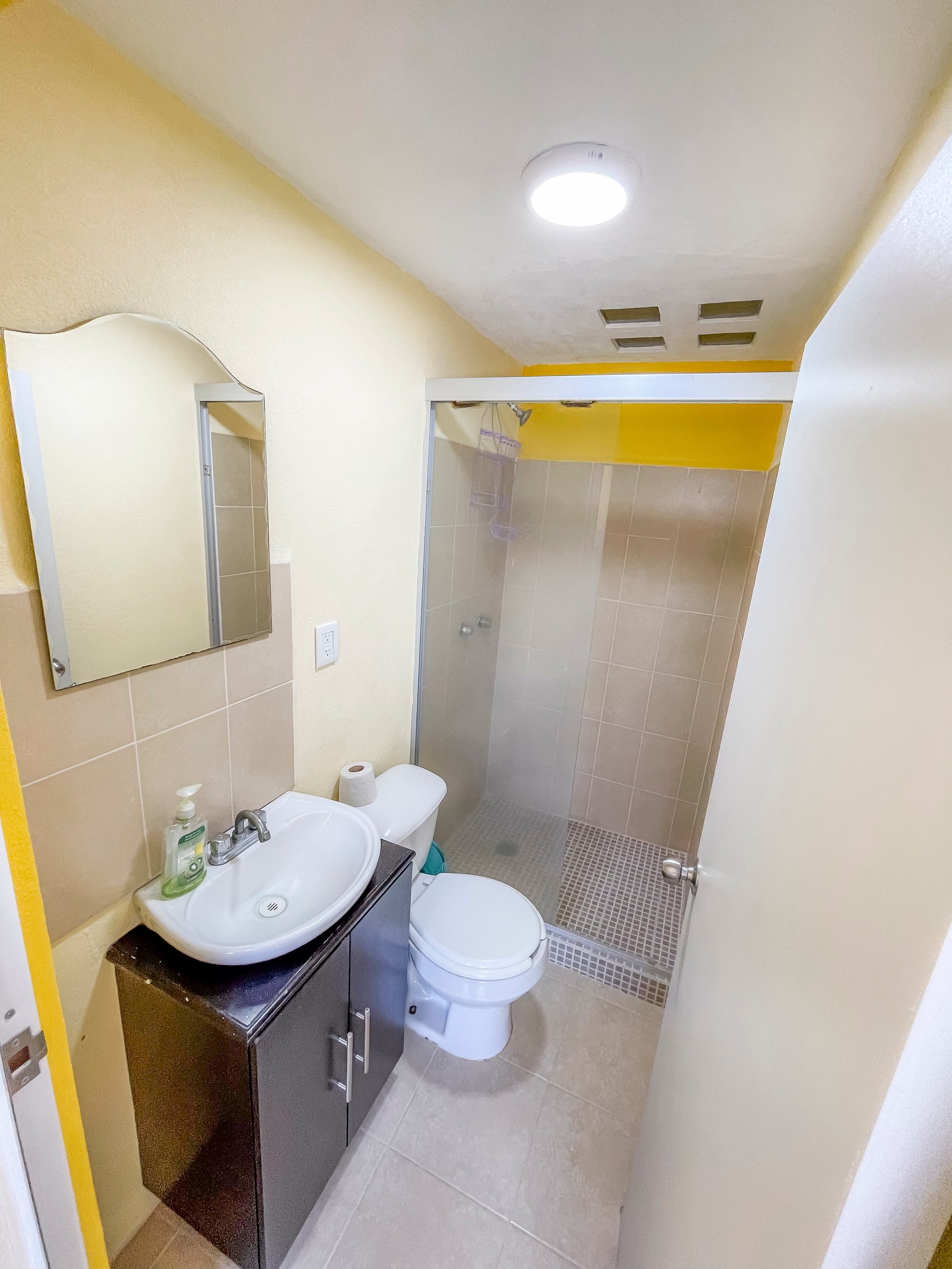 Modern bathroom with white tile walls, double sink vanity, toilet, and walk-in shower with glass enclosure