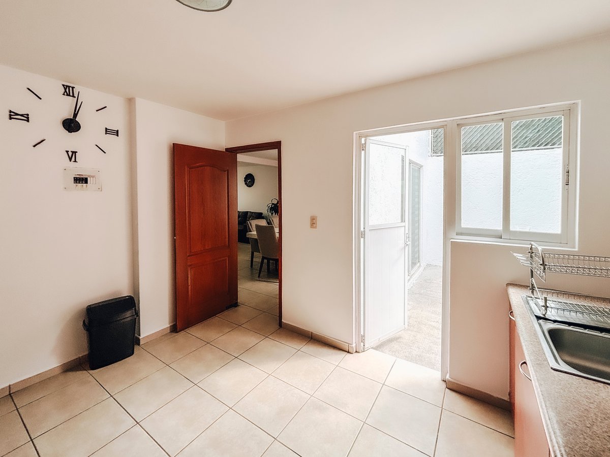 Modern kitchen with tile flooring, red door, wall clock, and glass doors leading to a balcony
