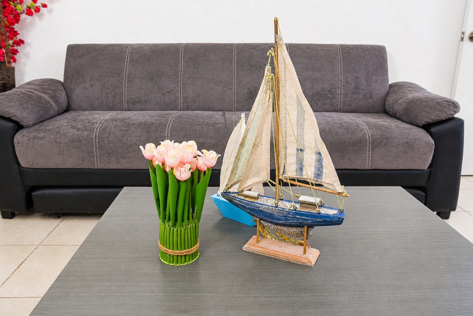 Living room with gray upholstered sofa, glass coffee table displaying a sailboat model and vase of pink flowers.