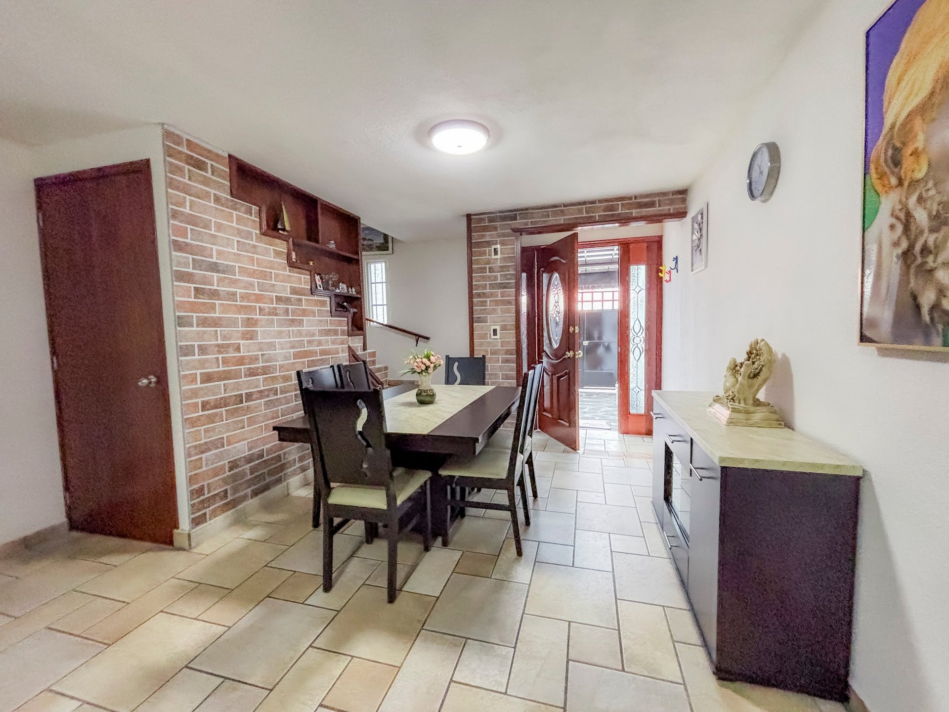 A spacious kitchen and dining area with brick walls, a round black dining table, chairs, and red doors leading to an entrance.