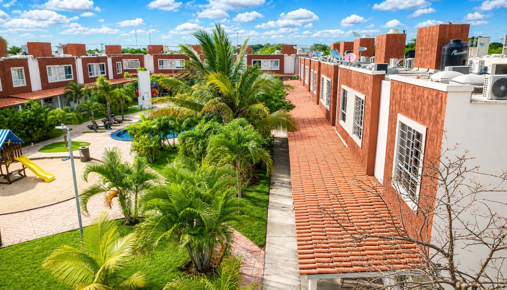 Aerial view of residential neighborhood with red brick townhouses, palm trees, and green courtyards under blue sky.