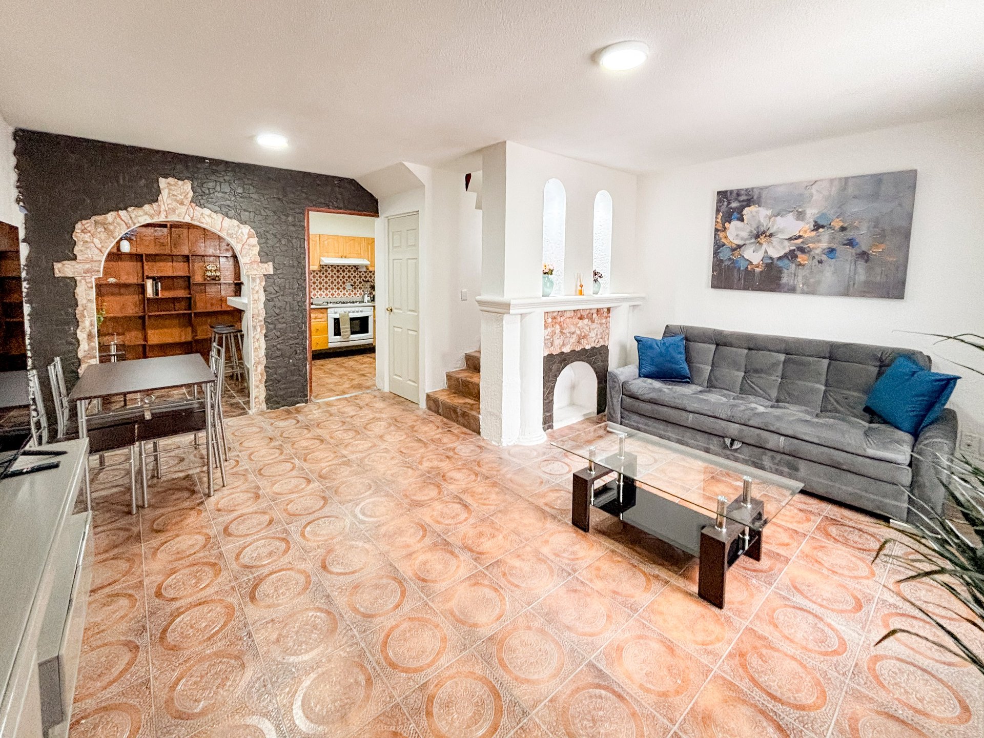 Modern living room with gray sofa, fireplace, arched alcove, beige geometric rug, and kitchen area visible in background