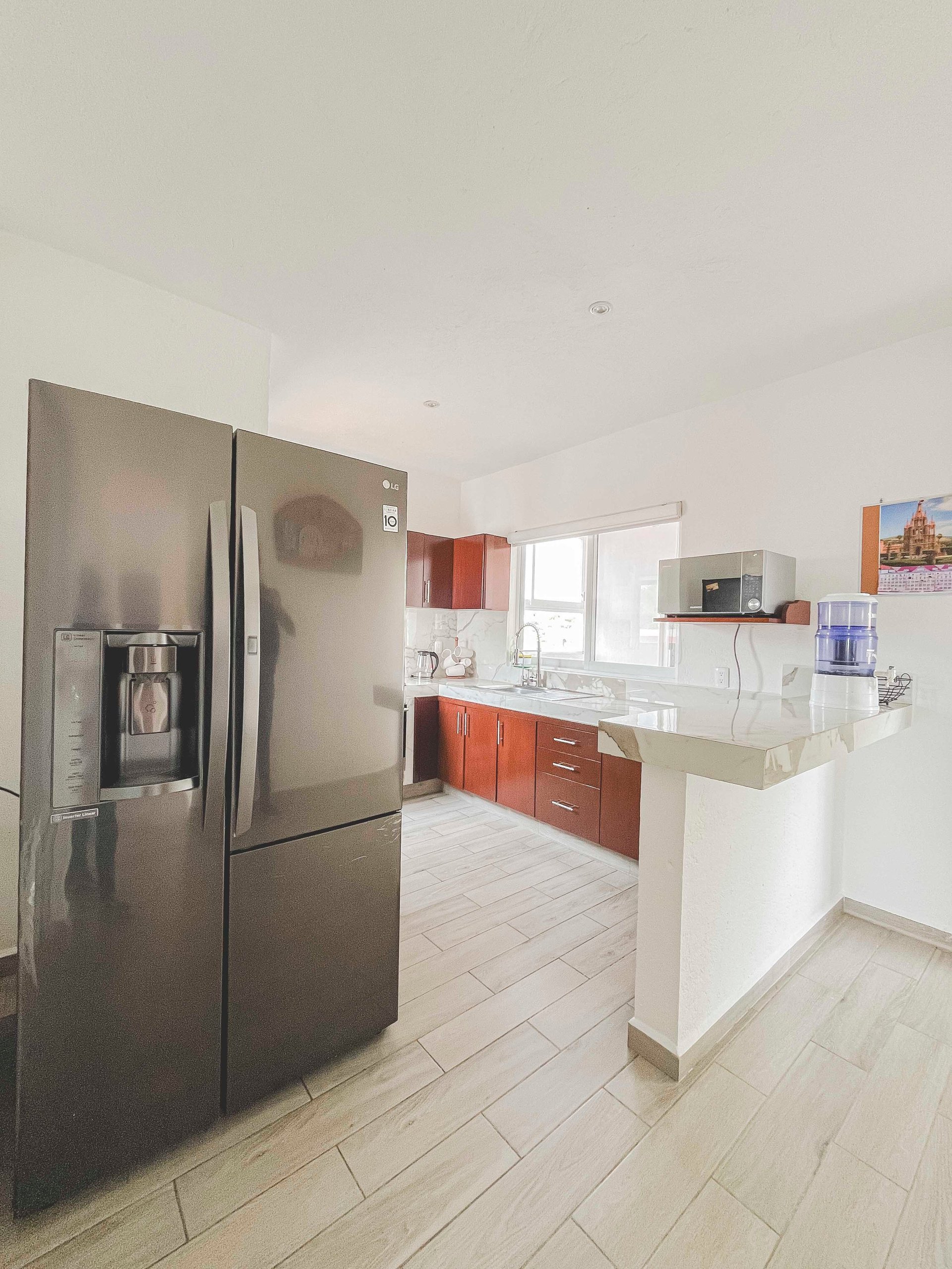 Modern kitchen with stainless steel French-door refrigerator, red cabinetry, white island, and light tile flooring
