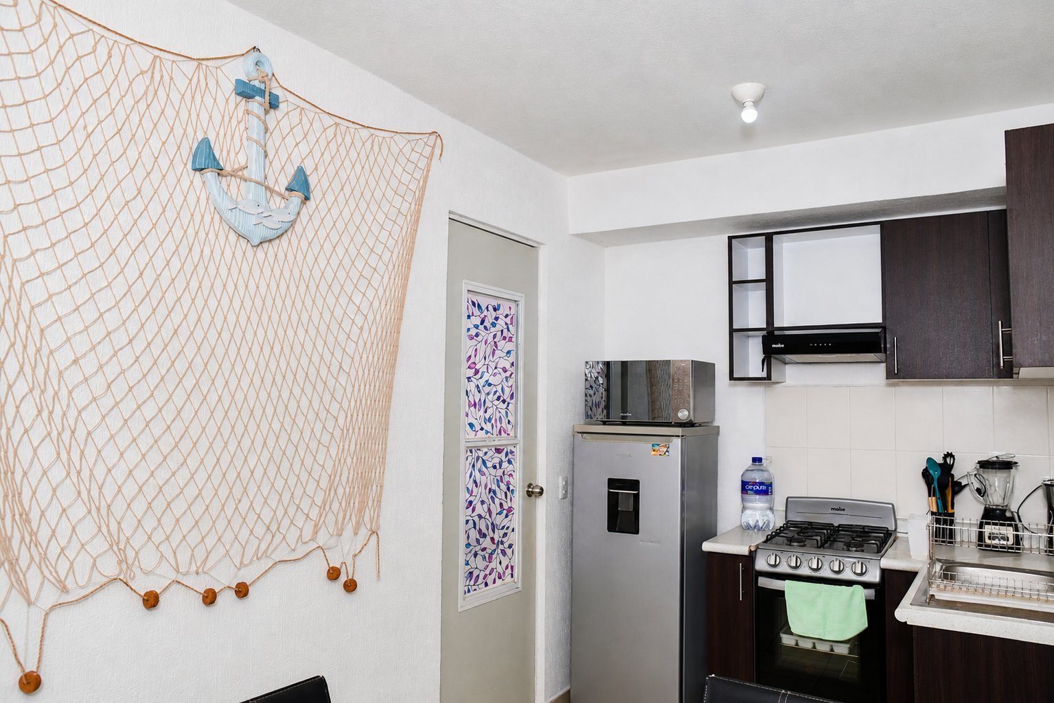 Modern kitchen with black and white cabinetry, stainless steel appliances, and nautical wall decor featuring a fishing net with anchor and sailboat design.
