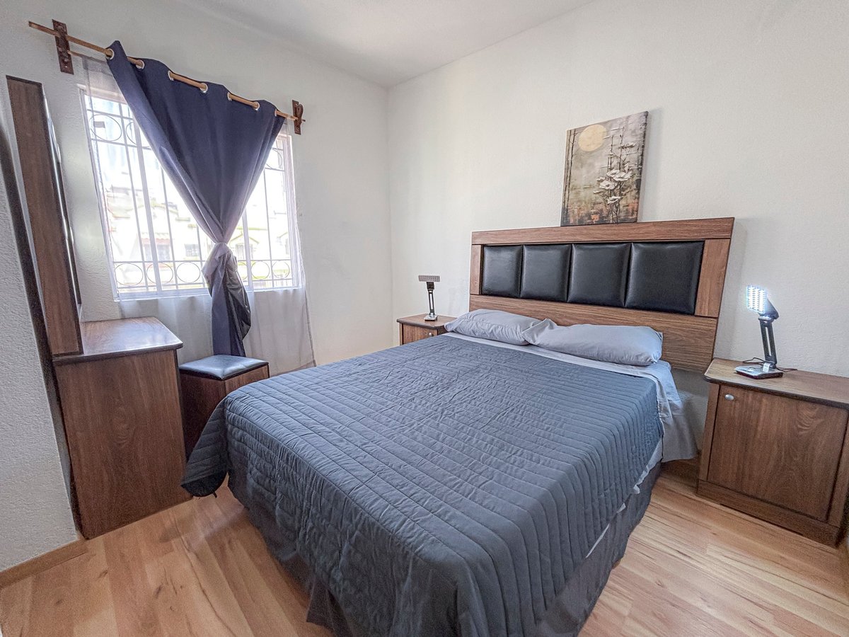 Modern bedroom with queen bed, wooden nightstands, and dark blue curtains on large window