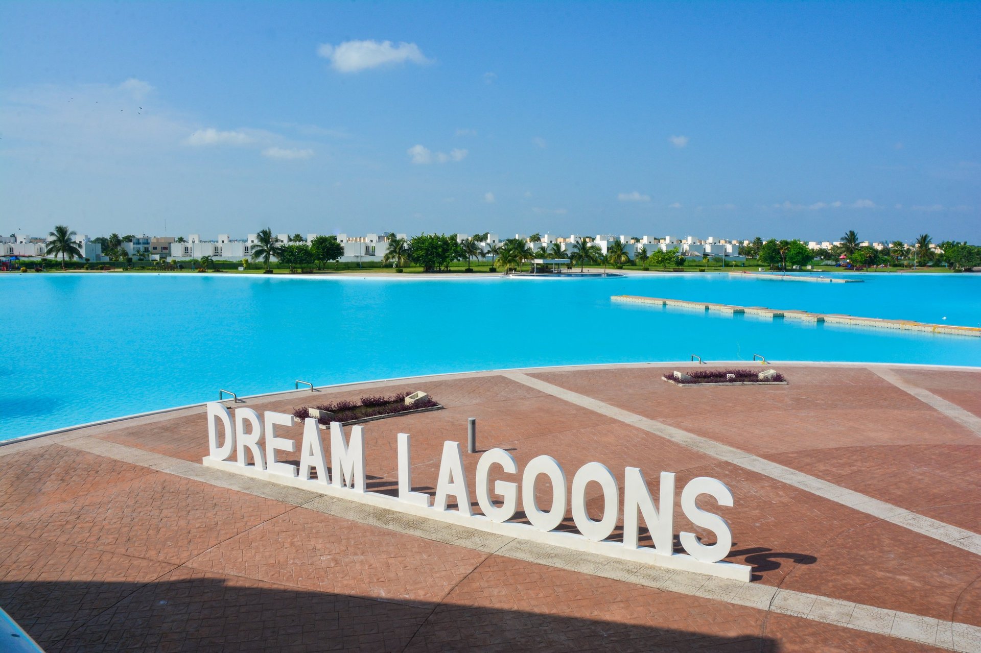 Dream Lagoons sign with turquoise water, sandy beach, and tropical vegetation under blue sky