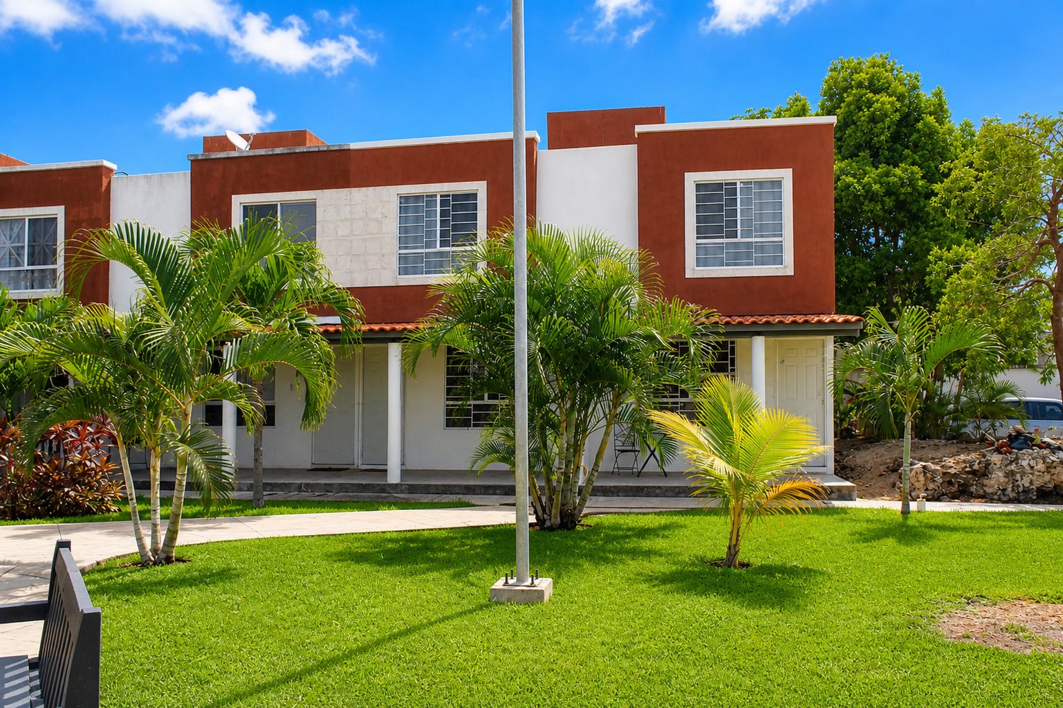 Modern townhouses with red-brick upper levels and white lower sections, surrounded by manicured green lawn and palm trees under blue sky
