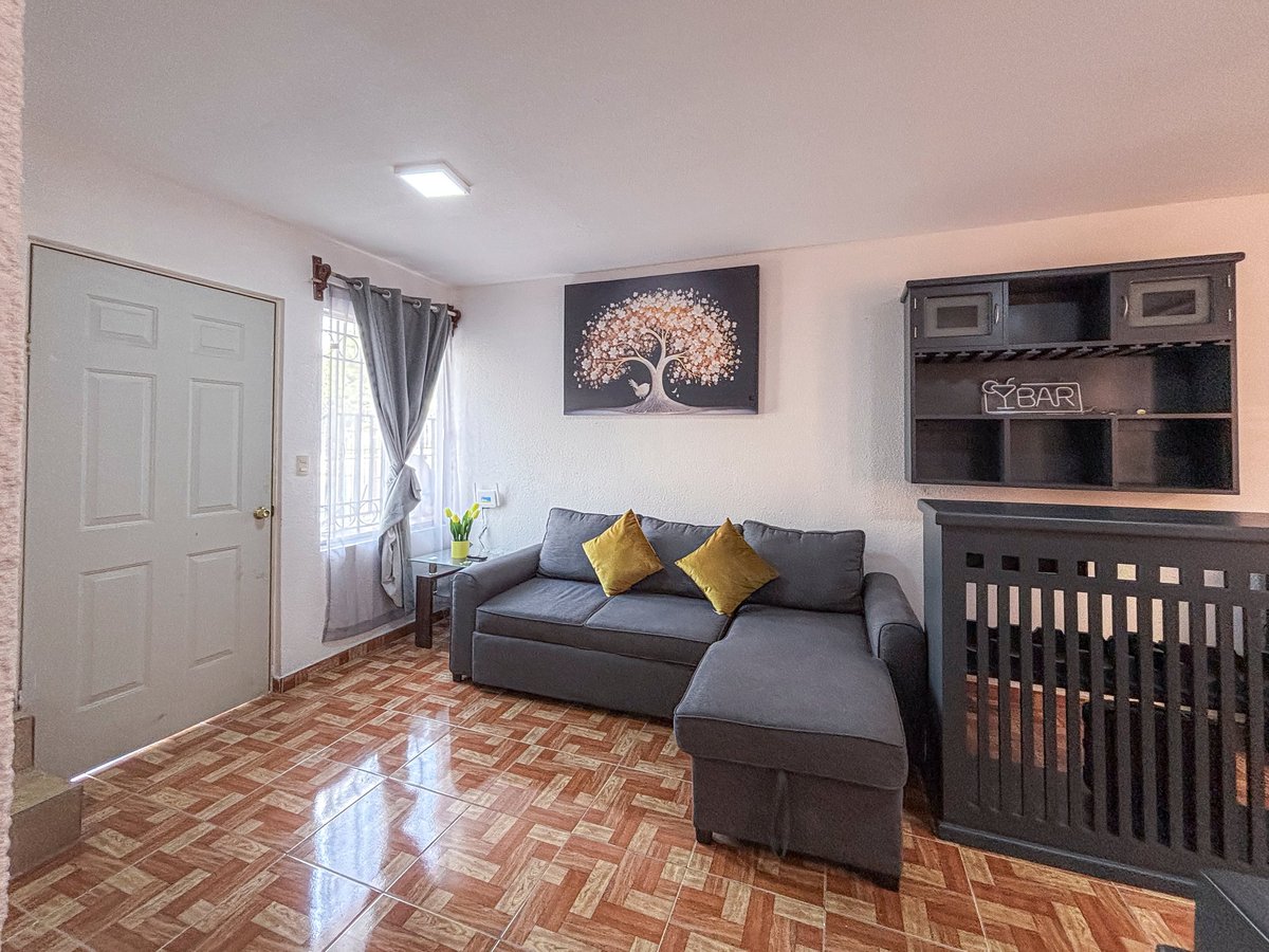 Modern nursery room with gray sectional sofa, wooden crib, tree artwork on wall, and parquet flooring