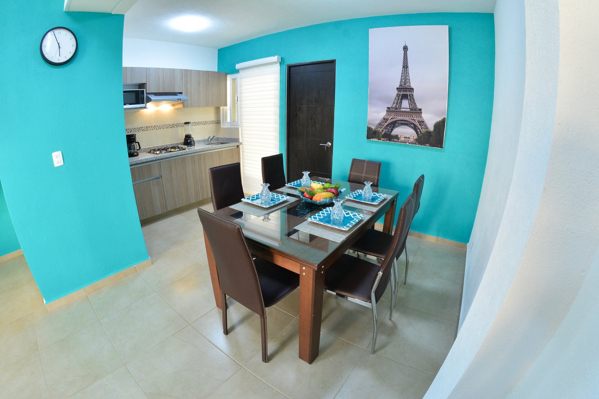 Modern apartment interior with turquoise walls, dining table with chairs, open kitchen area, and Eiffel Tower wall art