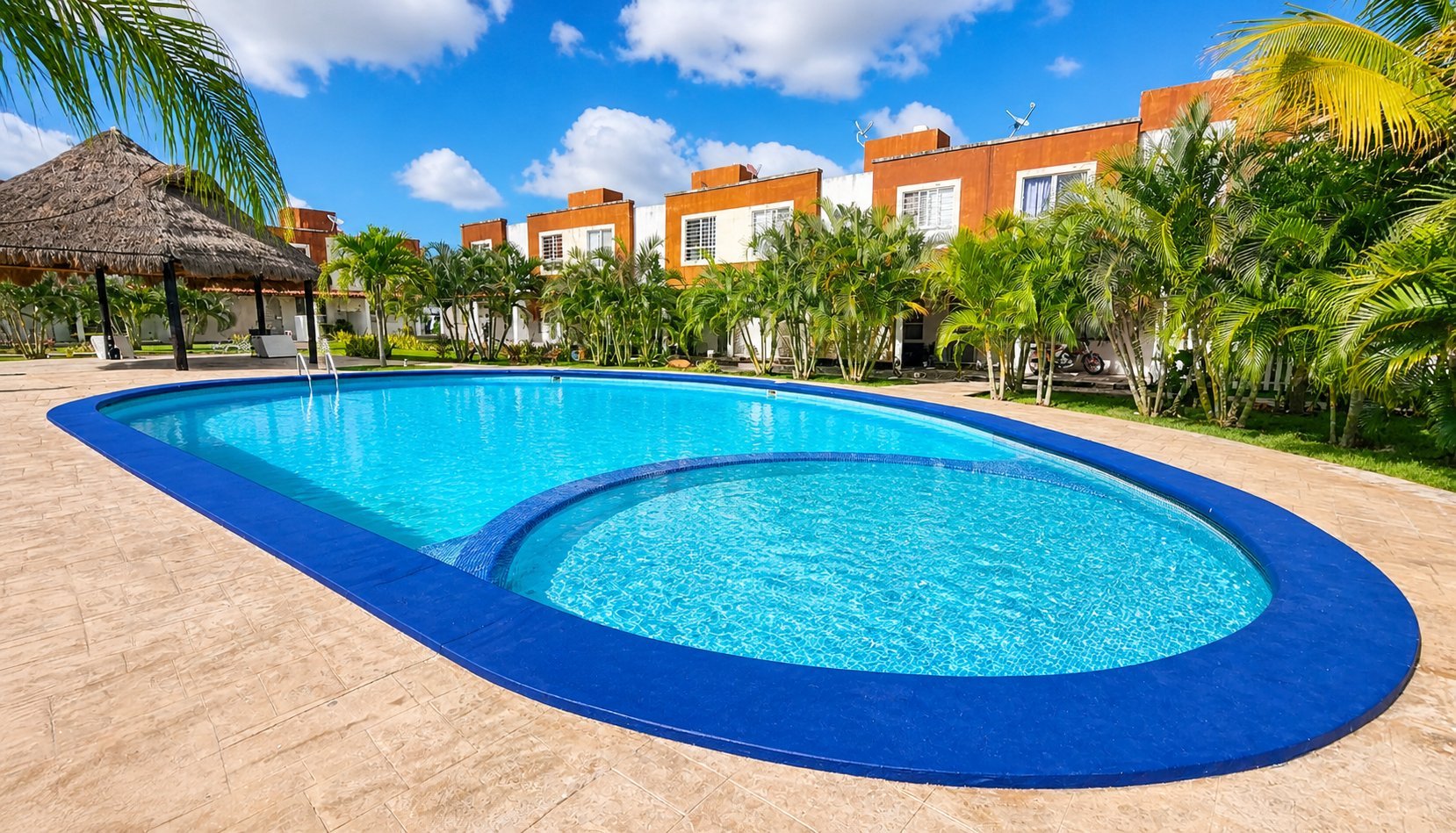 Luxury resort pool with blue water surrounded by palm trees, thatched palapa, and orange residential buildings under clear sky.