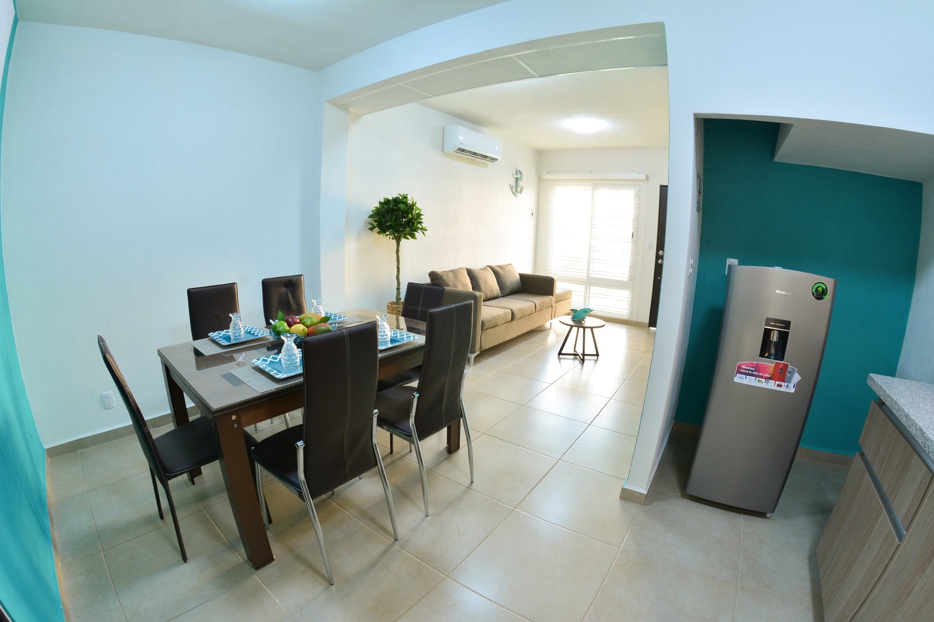 Modern open-plan apartment interior with dining table, sofa, stainless steel refrigerator, and turquoise accent wall