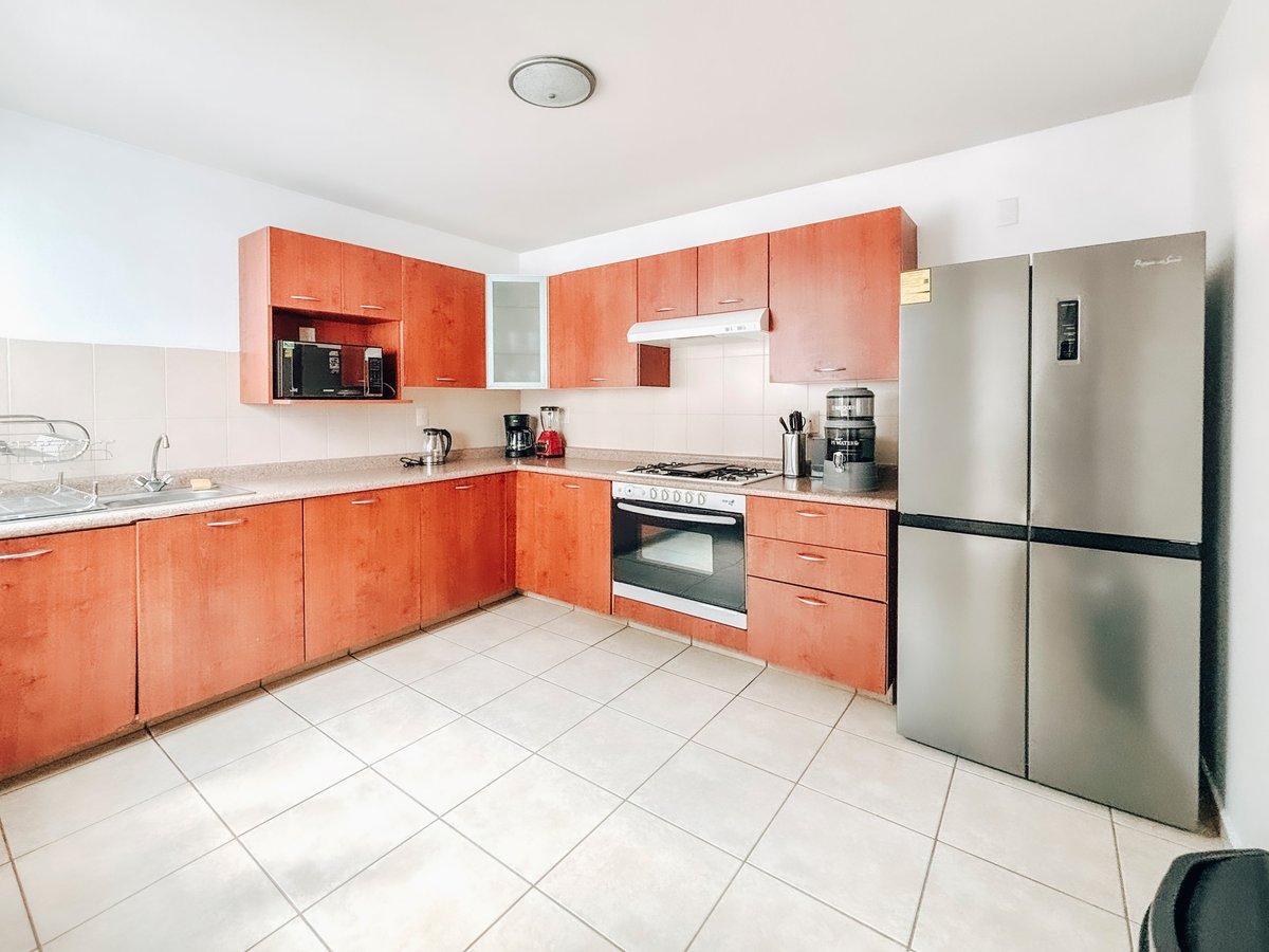 Modern kitchen with bright orange cabinetry, stainless steel appliances, white tile flooring, and white walls with recessed lighting.