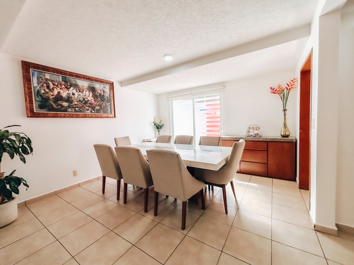 Modern dining room with beige upholstered chairs, glass table, tile flooring, and framed artwork on white walls