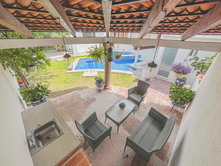 Covered patio with lounge chairs overlooking a backyard pool, plants, and landscaping