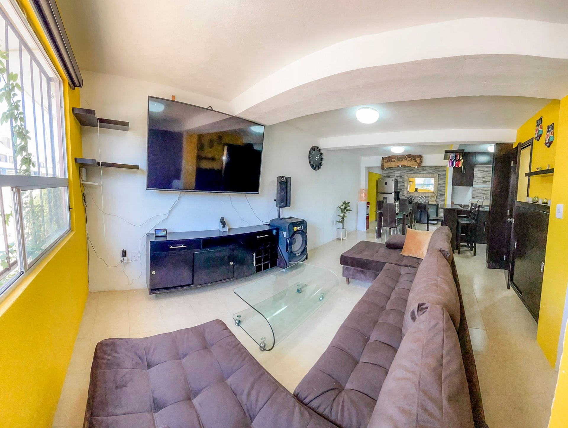 Modern living room with yellow walls, gray seating, wall-mounted TV, and curved ceiling with natural light from windows