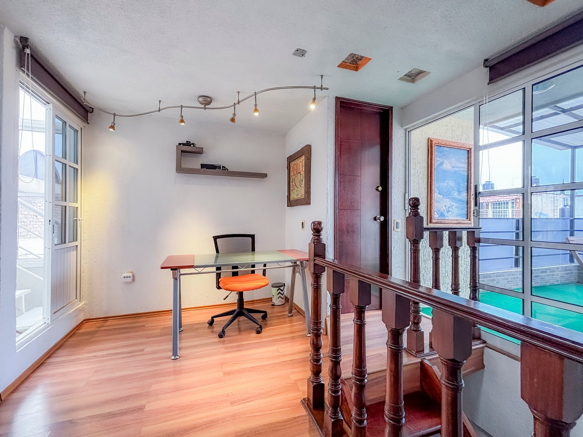 Modern loft office space with wood floors, orange desk chair, track lighting, and large windows overlooking a city skyline.