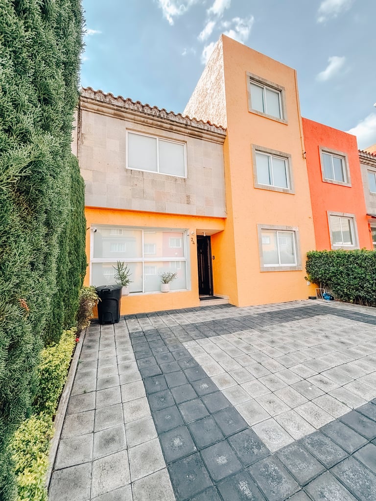Colorful modern townhouse with orange and beige facade, paved driveway, green climbing ivy, and blue sky