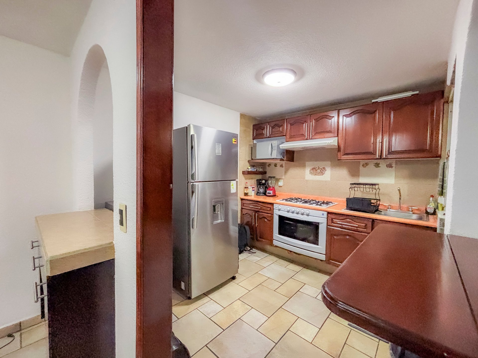 Modern kitchen with red cabinets, stainless steel appliances, tile flooring, and built-in workspace.