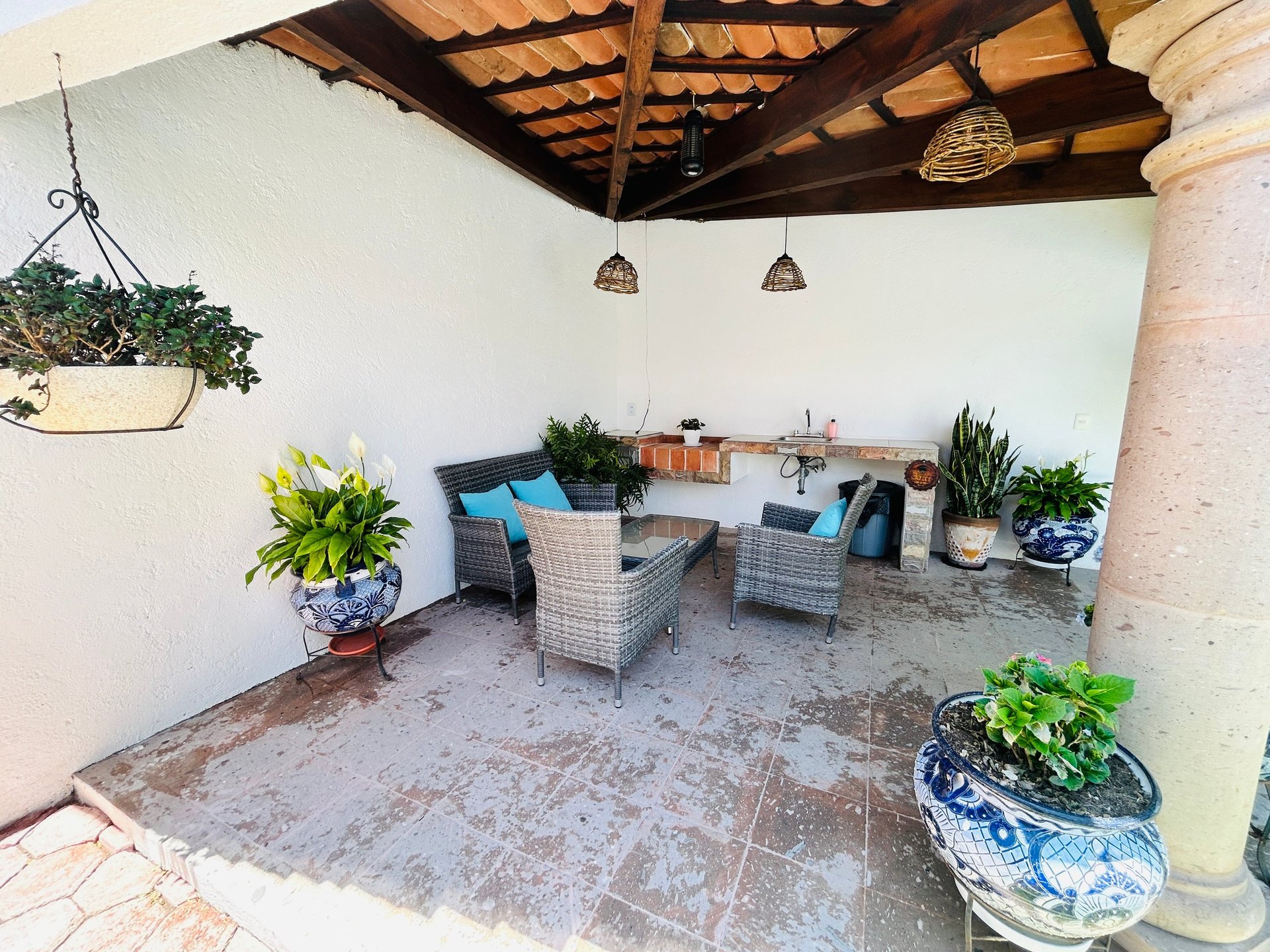 Outdoor patio area with wicker seating, potted plants, wooden ceiling beams, and pendant lights