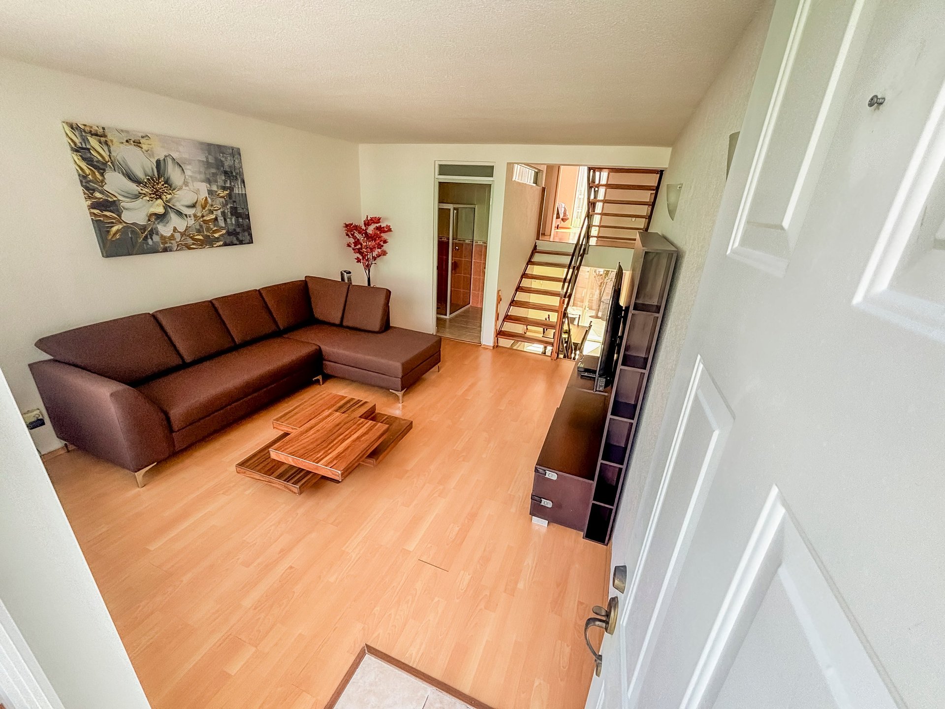 Modern living room with brown leather sectional sofa, wooden floor, and staircase visible in background