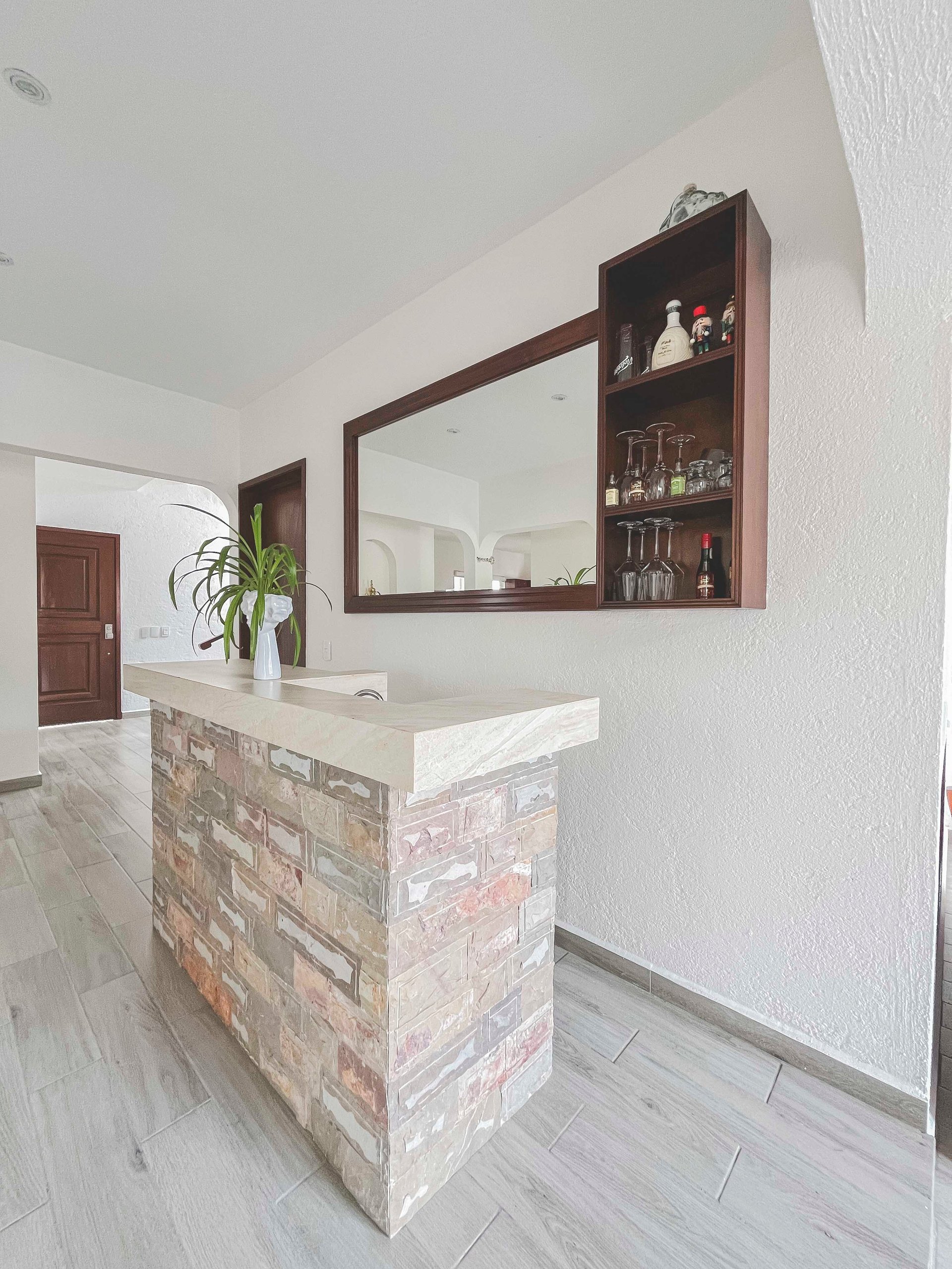 Modern bathroom vanity with brick base, marble countertop, large mirror with dark wood frame and shelving, white walls, and light wood flooring